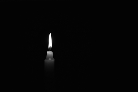 Light candle burning brightly in the black background. Candle flame. There's room for your text. Black and white photo. The concept of mourning, grief or sorrow. Located on the left side of the shot.の写真素材