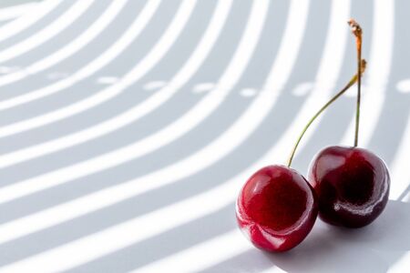 two cherry on white background illuminated by the rays of the sun from the window passing through...