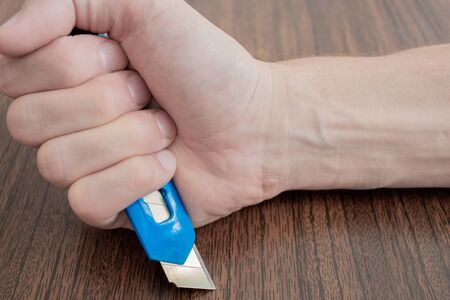 office knife in hand. shallow depth of field. hands are placed on brown background. the concept of...