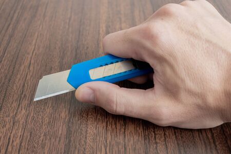 office knife in hand. shallow depth of field. hands are placed on brown background. the concept of depression and suicide.の写真素材