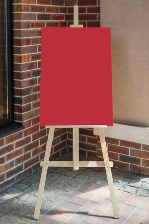 Wooden Artist Easel with Red Blank Mockup Poster for Your Design in front of Brick Wallの写真素材