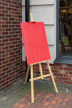 Wooden Artist Easel with Red Blank Mockup Poster for Your Design in front of Brick Wallの写真素材