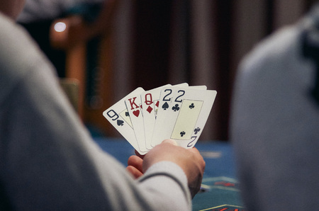 casino, gambling, poker, people and entertainment concept - close up of poker player with playing cards and chips at green casino table over holidays lights backgroundの写真素材