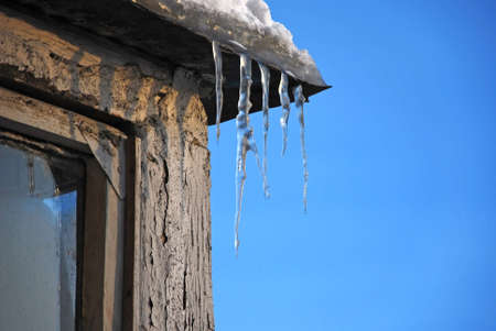 Large icicle formed at the end of roof against clear blue skyの写真素材