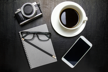 Top view of office desk workspace with coffee cup, notebook, camera, pencil ,mobile phone ,glasses on wooden backgroundの写真素材