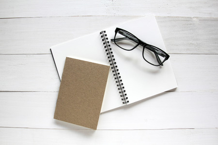Notebook and glasses on white wooden table background.の写真素材