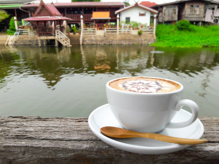 A hot latte coffee cup on wooden table beside the river.の写真素材