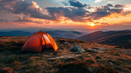An illuminated tent stands on a mountain ridge against the backdrop of a stunning sunset, with sweeping views of layered mountain ranges.の素材
