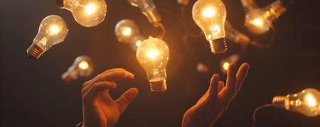 This vibrant image depicts a hand deftly juggling a collection of illuminated light bulbs each representing a unique idea or creative spark The bulbs warm radiant glow symbolizes the illumination andの素材