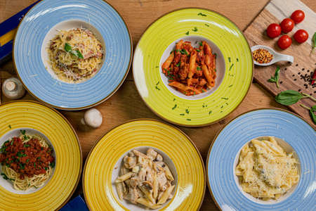 Several plates of pasta & spaghetii with different kinds of sauce over wooden background, top view. Concepts of Italian food.の写真素材