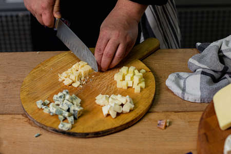 Chef hands cutting parmesan cheese on wooden board in the kitchen. Concept of cheese collection and...
