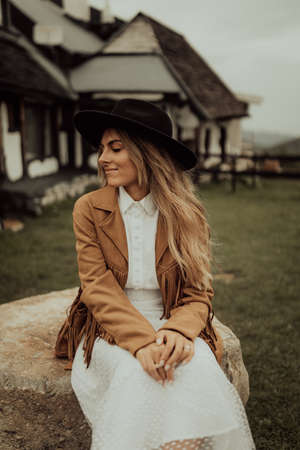 Young bride dressed in boho style with boots and hat, enjoying the sun in a breathtaking mountain landscape.の写真素材