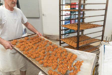 The baker places the fresh salted pretzels taken out of the oven.Trays with many pretzels in the...