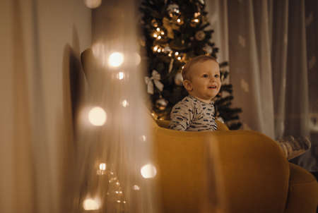 Happy child sits on an armchair with decoration and Christmas tree in the background.の写真素材