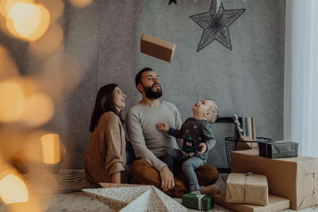 Man and woman and their child celebrate Christmas holidays together, embracing and playing with gift...