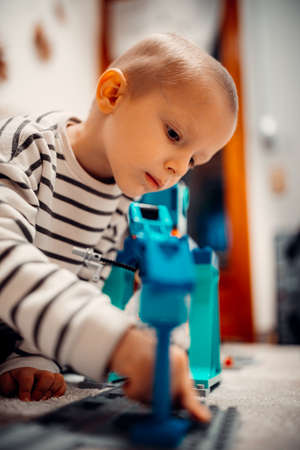 A happy kid playing with plastic train on toy railway road at home.の写真素材