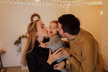 The little girl held in her father's arms is playing with a light from a Christmas decoration