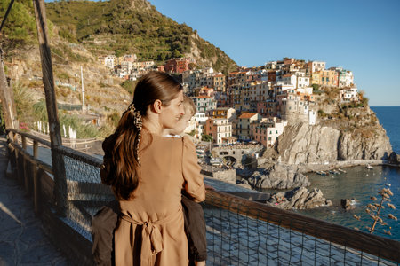 A beautiful woman holding her little child in her arms, admiring the colorful village of Manarola in...