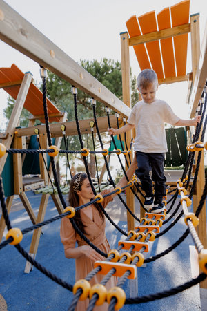 A happy little boy is playing on a rope bridge in the park, with the help of his mother.の写真素材