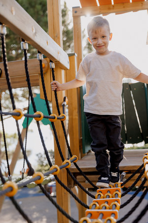 A happy little boy is playing on a rope bridge in the park, with the help of his mother.の写真素材
