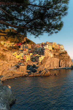 picturesque fishing village of Manarola, located on the rugged coast of the Liguria region in Italy, with colorful houses perched on steep hills that slope down to the sea, a small harbor with fishing boats or pleasure crafts, and the vast blue sea stretching into the horizon.の写真素材