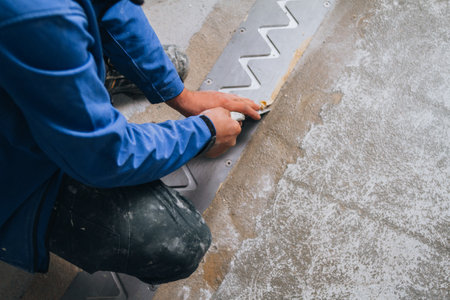 worker's skilled hands installing floor expansion joints. The worker is shown wearing protective gear and kneeling down on the concrete floor, using specialized tools to carefully measure and cut the material to fit precisely.の写真素材