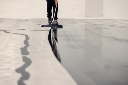 Worker applies grey epoxy resin to a new floorの写真素材
