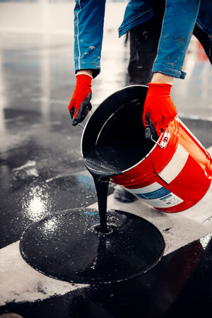 Man pours epoxy resin from a bucket to the new floor for coatingの写真素材