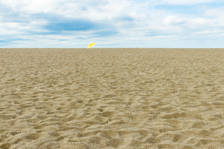 Sand dunes on the beach with a yellow umbrella in the foregroundの写真素材