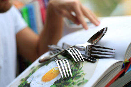 Kitchenware on the book with recipes, fork and spoonの写真素材