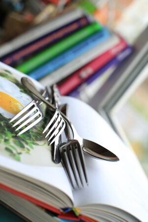 Kitchenware on the book with recipes, fork and spoonの写真素材