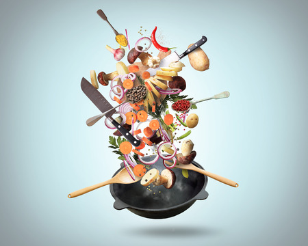 Large iron skillet with falling vegetables and mushroomsの写真素材