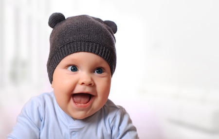 Baby in the hat smiling while sitting in bedの写真素材