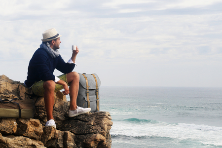 Traveler drinking coffee against the waves of the oceanの写真素材