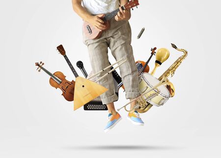 Young man jumped up playing guitar among musical instrumentsの写真素材