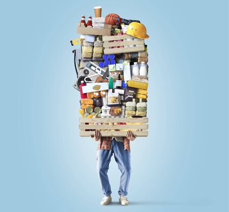 Man is holding a huge pile of food and other goodsの写真素材