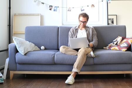 Young man sitting and working on sofa with laptop, business concept