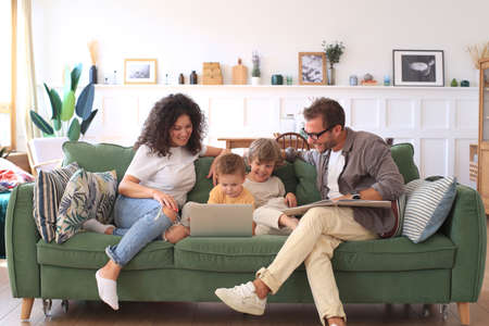 Young beautiful happy family relaxing on the sofa and look at the laptop at home.の写真素材