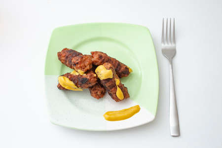 Romanian , traditional meat rolls, called âmiciâ or âmititeiâ with mustard   on a green ceramic plate, isolated on whiteの写真素材