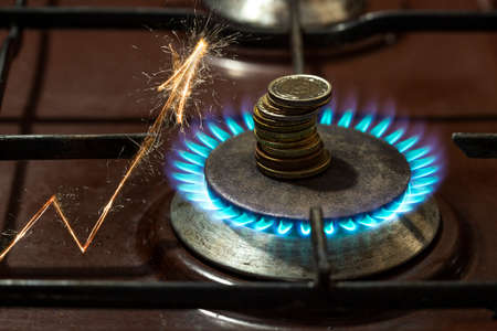Defocused gas burner with coins and flames, and an arrow made with fireworks representing gas prices