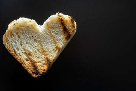heart shaped grilled slice of bread, macro of toast isolated on black, with a lot of copy space....