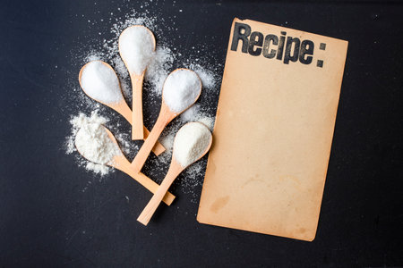 Recipe stamped on a vintage paper page on black  background next to bamboo spoons with white spicesの写真素材