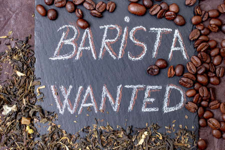 Barista wanted written with chalk on a black stone tile, surrounded by coffee beans and green Jasmin tea leavesの写真素材
