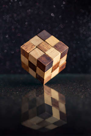 wooden rubik's cube standing in equilibrium on the edge on a reflective black glassのeditorial素材