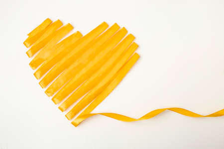 heart shape made with silky golden  satin tape. Yellow heart on white backgroundの写真素材