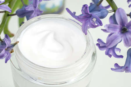 Cosmetic cream texture in a glass jar, next to purple flowersの写真素材
