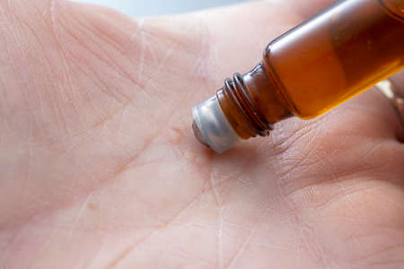 little roll on container with essential oil, on a hand palm, shallow depth of field close up