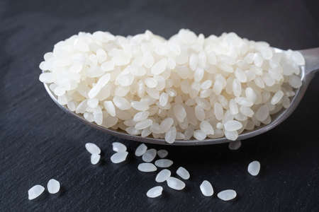 spoon full of white rice isolated on a black stone tile, close upの写真素材