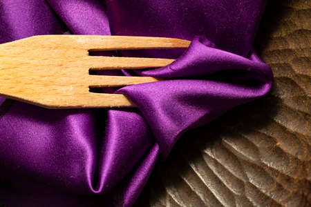 wooden fork and purple satin on a sculpted rustic plate, close up