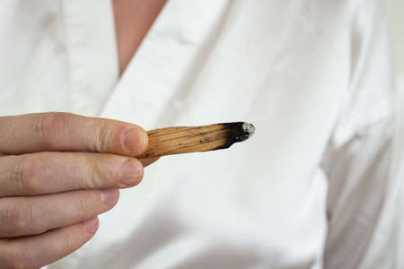 woman hand holding a stick of sacred palo santo wood, burning. white satin background.の写真素材